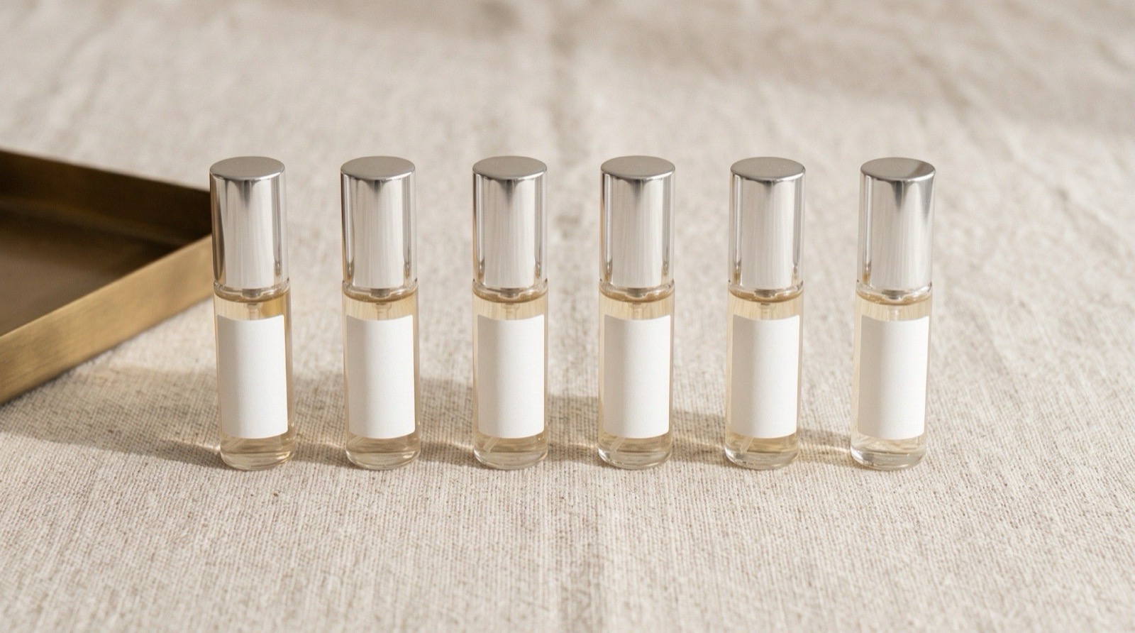 A row of identical clear-glass 5 ml atomizers spaced evenly on a linen surface, all the same size and finish